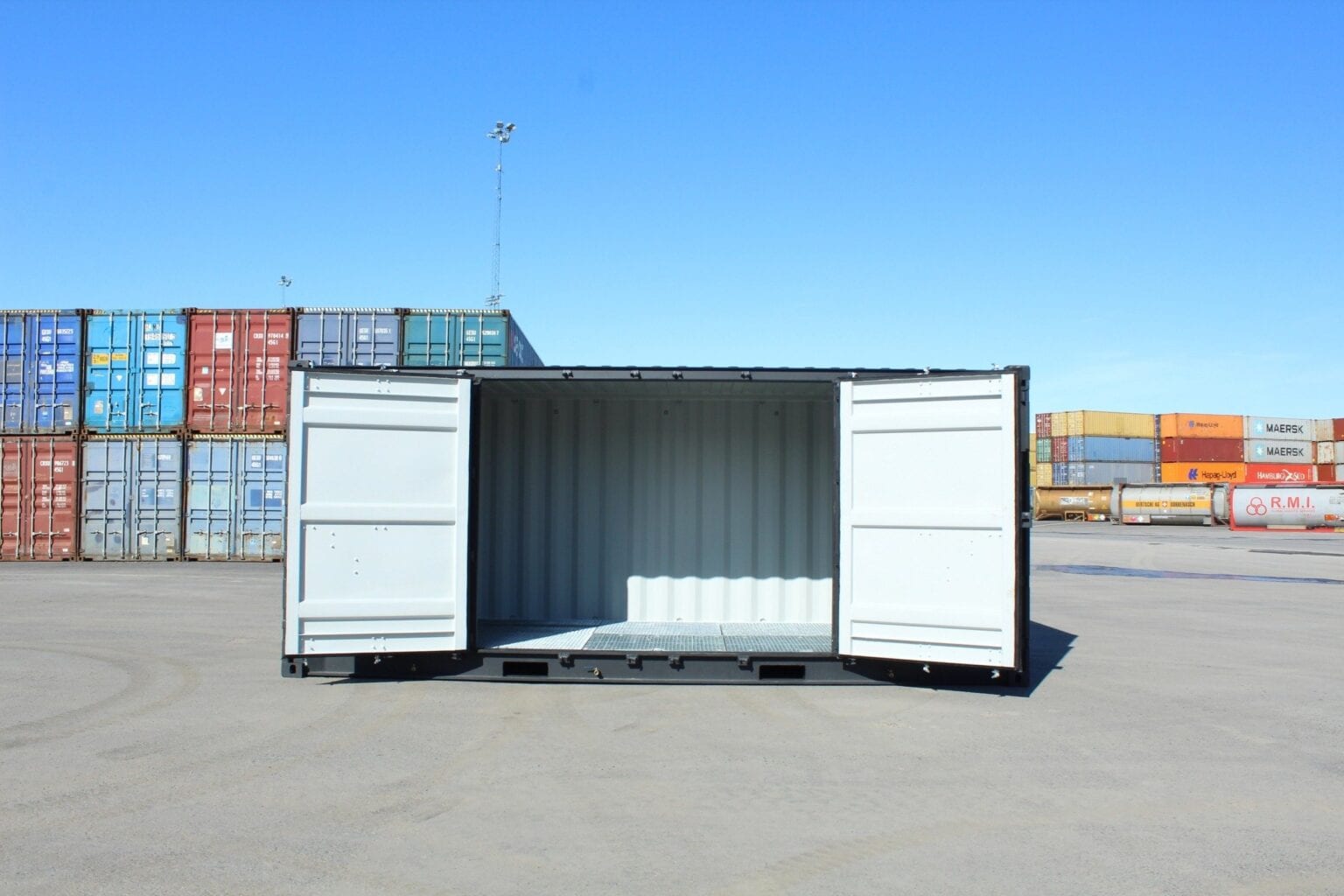 Open-sided shipping container in front of stacked containers at a port